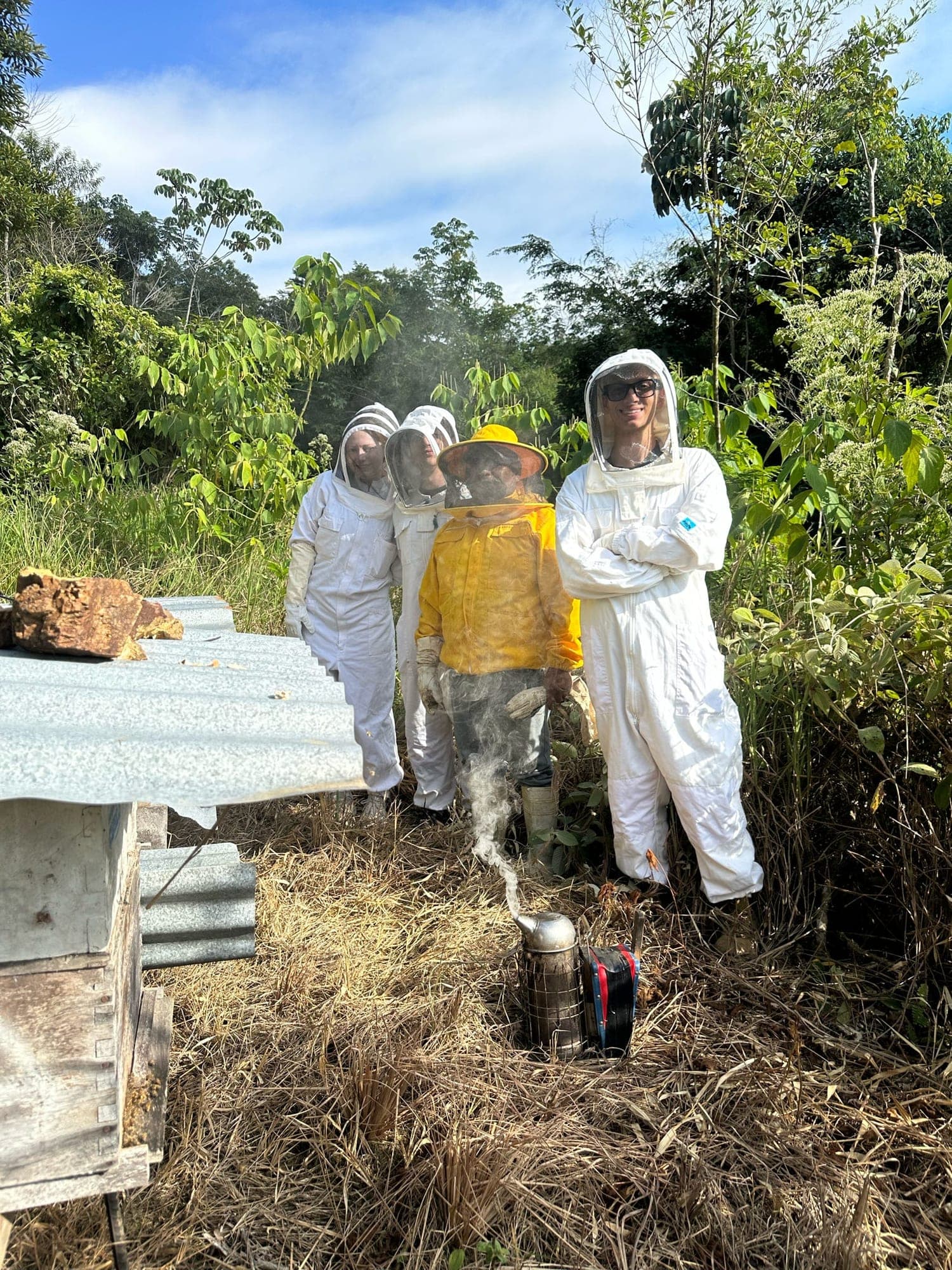 Me and two coworkers in beekeeping suits, standing with a local beekeeper.