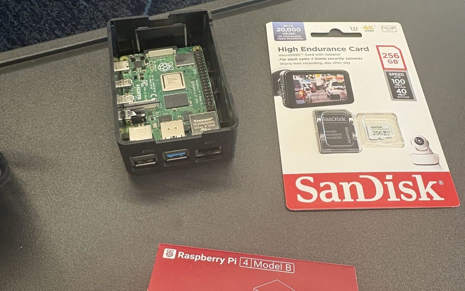 A Raspberry Pi 4 Model B seated in an open black case, beside a 256GB microSD card in its packaging and the Raspberry Pi retail box.
